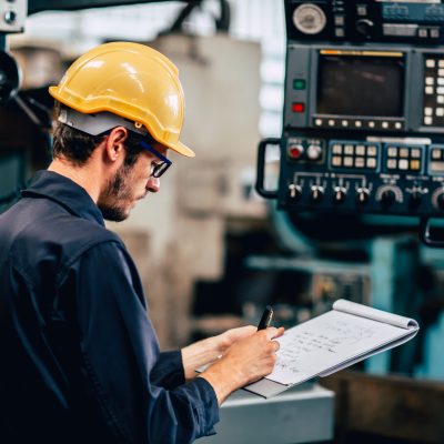 young profession technician engineer operate heavy machine to automated CNC in factory, worker with check list.